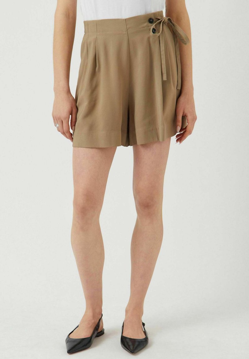 Khaki plyschorts med hög midja, sidband och två framknappar, tillverkade av ett mjukt tyg. Matchade med svarta spetsiga ballerinas.