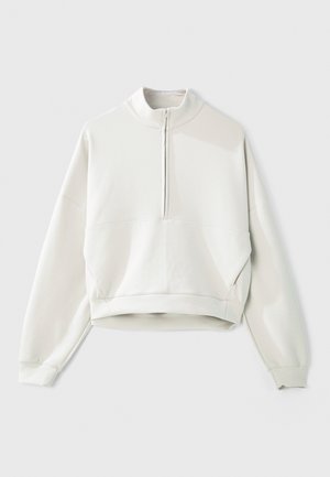 Heleroheline lühendatud pusa kõrge krae ja veerandlukuga, millel on pikad varrukad ja pehme, sile tekstuur.