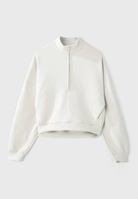 Svetlo siva majica s visokim ovratnikom, polu-zatvaračem sprijeda, spuštenim ramenima i rebrastim manžetama. Mekan materijal i skraćeni dizajn.