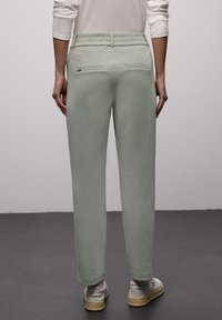 Pantalon vert clair, coupe décontractée, avec une ceinture élastique, des poches arrière et une texture douce, associé à des baskets gris clair.