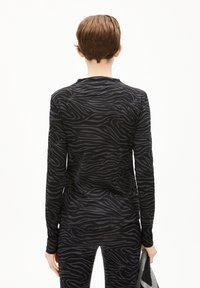 Schwarzes Langarmoberteil mit grauen Zebra-Streifen und tailliertem Schnitt, kombiniert mit passenden Leggings, gehalten mit einem grauen Accessoire.