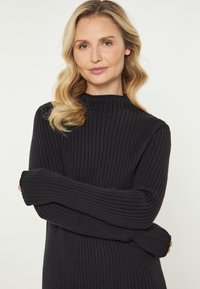 Pulover negru din tricot cu voaluri, având guler înalt și mâneci lungi, cu un material texturat și o siluetă ajustată.