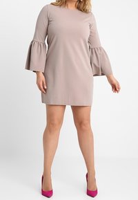 Robe beige à manches courtes avec des manches évasées et une coupe droite, associée à des chaussures à talons fuchsia. Texture lisse, design minimal.