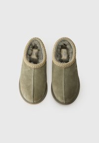 Pantofole in suede verde con forma arrotondata, foderate in pelliccia testurizzata e con un dettaglio ricamato dorato lungo il bordo superiore. Logo UGG visibile all'interno.