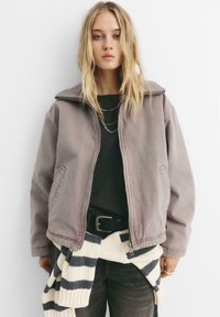 Grå, oversized jakke med ribbet krave, lynl�åslukning foran og sidelommer. Laget over en sort skjorte og suppleret med en stribet striktrøje.