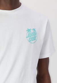 White cotton t-shirt featuring a circular turquoise graphic with palm trees and the text "SANTA CRUZ" on the left chest area.