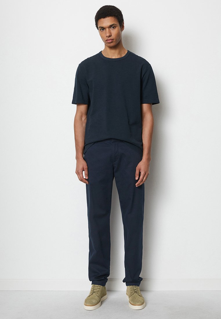 Granatowa bawełniana koszulka z okrągłym dekoltem, zestawiona z ciemnogranatowymi spodniami i jasnooliwkowymi sneakersami, charakteryzująca się luźnym krojem.