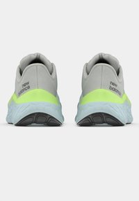 Sapatilhas de corrida da New Balance em cinza e verde néon, vistas pela parte de trás, com solas azuis grossas e piso preto.