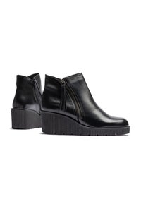 Black leather wedge ankle boots with a side zipper and tassel detail. Textured rubber sole with horizontal grooves. Rounded toe design.