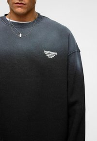 Zwarte sweatshirt met een ronde hals, een relaxte pasvorm en een textuurstof. Geborduurd logo in het wit op de bovenste linkerborst.