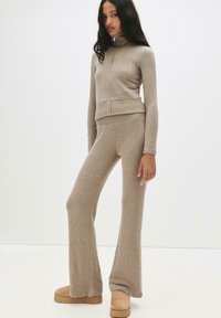 Beige strik lounge sæt med en lynlås-op mock neck top og flagrende bukser. Blød tekstur med ribbede detaljer og en afslappet tætsiddende design.