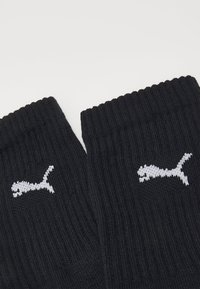 Schwarze gestrickte Socken mit gerippter Struktur, ausgestattet mit einem weißen Logo am Bund. Das Design umfasst eine nahtlose Spitze und ein elastisches Obermaterial.