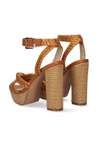 Las sandalias de plataforma trenzadas en color marrón presentan un diseño de tiras texturizadas, una correa de tobillo con hebilla y tacones gruesos envueltos en paja.