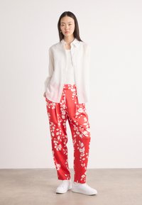 Hvit skjorte med knapper, hvit tank top, røde blomsterbukser og hvite sneakers. Buksene har en glansfull tekstur og dristige hvite blomster mønstre.