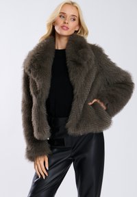 Kurtka z sztucznego futra w stonowanym odcieniu szaro-brązowym. Posiada szeroki kołnierz, miękką teksturę oraz skrócony krój. W połączeniu z czarnymi spodniami.