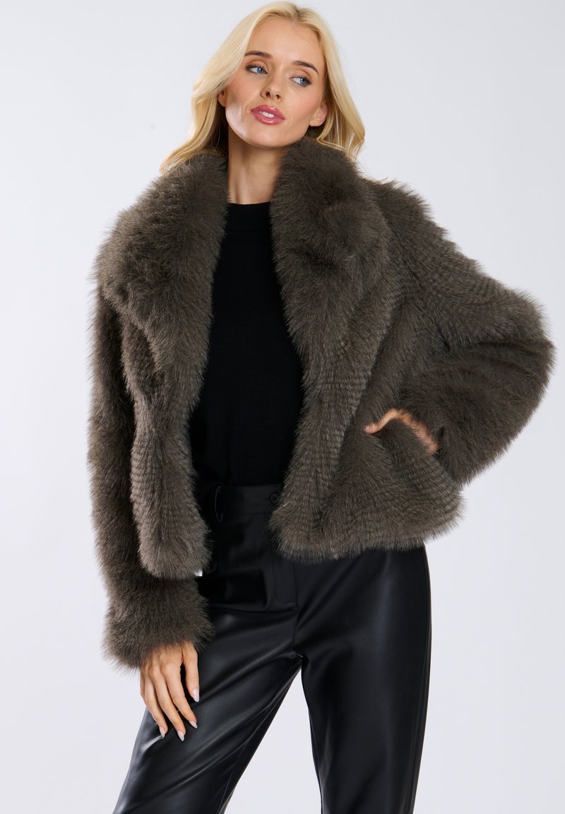 Kurtka z sztucznego futra w stonowanym odcieniu szaro-brązowym. Posiada szeroki kołnierz, miękką teksturę oraz skrócony krój. W połączeniu z czarnymi spodniami.