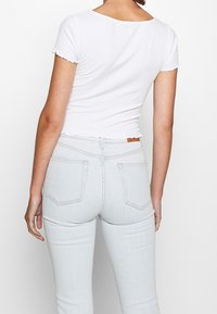 Vit ribbad topp med korta ärmar och en vågig fåll, i kombination med ljusblå jeans med bakfickor och en läderetikett.