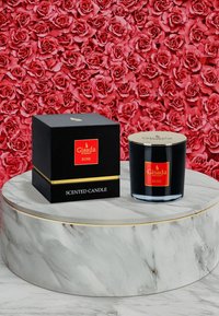 Schwarze Glasduftkerze mit einem goldenen Deckel und rotem Etikett. Quadratische schwarze Schachtel mit der Aufschrift "Duftkerze" und goldenen Akzenten, auf einem Marmorständer platziert.