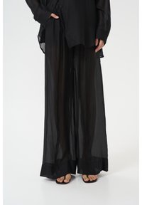 Combinaison d'une chemise noire en voile surdimensionnée et d'un pantalon large, mettant en avant un tissu léger et translucide avec une texture subtile, et une coupe décontractée.