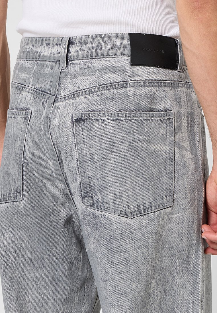 Lichtgrijze denim jeans met een verouderd patroon, met achterzakken en een zwart leren label op de tailleband.