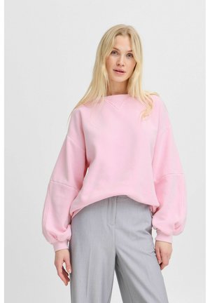Pink sweatshirt with oversized sleeves, ribbed cuffs, and a round neckline, worn with light gray tailored trousers. Smooth, soft fabric.