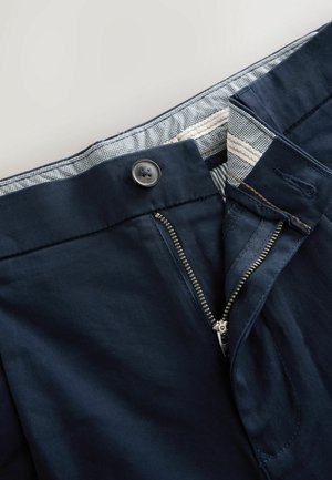 Mornarsko modri hlače z zadrgo in gumbnim zapiranjem, ki imajo teksturiran pas z karirastim vzorcem.