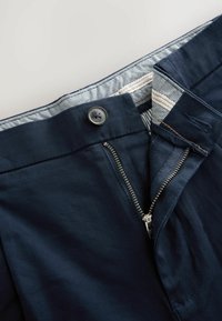 Granatowe spodnie z przednim zamkiem błyskawicznym, zapięciem na guzik i kratkowanym paskiem w talii. Charakteryzują się gładką fakturą i wytrzymałą tkaniną.