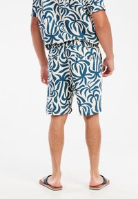 Korte mouwen shirt en bijpassende korte broek met een blauw en ivoorkleurig bladenpatroon, gemaakt van lichtgewicht stof en voorzien van een elastische tailleband.