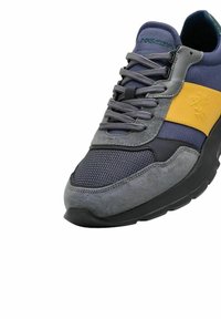 Zapatilla atlética gris con una banda de acento amarilla, materiales de malla y ante, puntera redondeada y suela de goma texturizada. Cordones en gris.