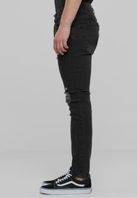 Jeans skinny negros con detalle desgastado en las rodillas, fabricados en algodón, de corte slim, y acompañados de zapatillas negras de corte bajo con acentos blancos.