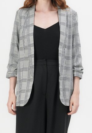 Grå ternet blazer med op rullede ærmer, åben front, har et tekstureret stof og en kontrasterende sort inderside. Båret over en sort bluse.