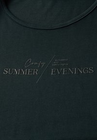 Mörkgrön t-shirt med rund halsringning. Har präglad text som läser "Bekväma SOMMAR / KVÄLLAR" och "solkyssta och milda nätter." Slät yta.