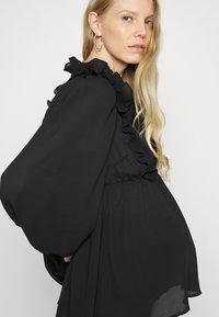 Blusa preta com detalhes franzidos ao longo do decote e das mangas, com um corte descontraído e tecido suave e leve.