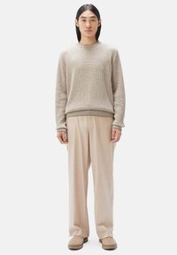 Beige Strickpullover mit Rundhalsausschnitt, kombiniert mit hellbeigen Hosen. Das Outfit hat eine lockere Passform und eine weiche Textur.