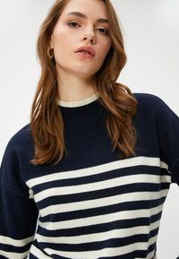 Marineblauwe trui met witte horizontale strepen, geribbelde halslijn en lange mouwen; zachte textuur; casual, ontspannen pasvorm.