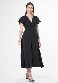 Vestido negro con mangas cortas y volantes, escote en V y detalle frontal retorcido. Llega hasta la mitad de la pantorrilla, hecho de una tela suave.