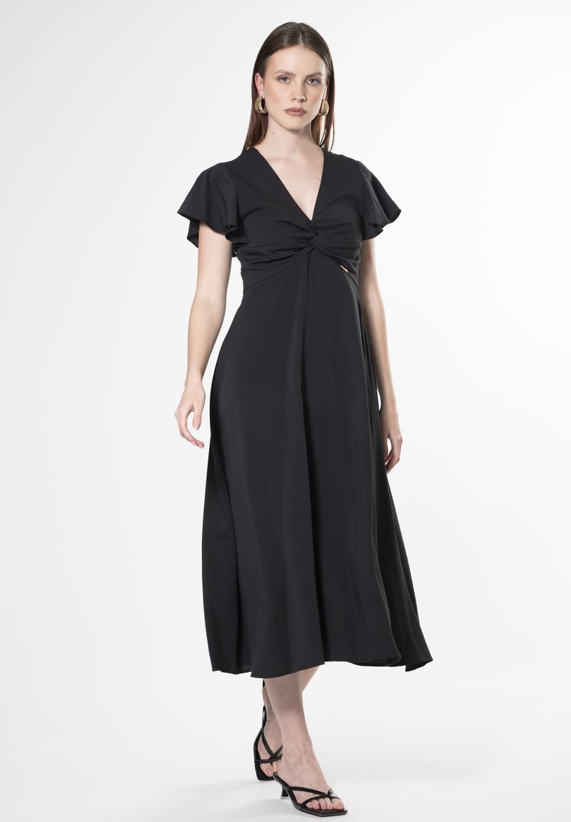 Vestido negro con mangas cortas y volantes, escote en V y detalle frontal retorcido. Llega hasta la mitad de la pantorrilla, hecho de una tela suave.