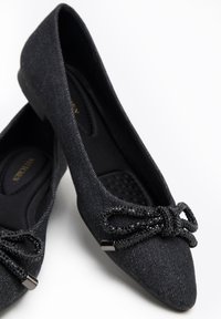 Zwarte stoffen ballet flats met een gestructureerde afwerking, voorzien van een decoratieve strik met zwarte kralen en een lage, afgeronde hak.