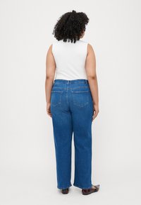 Zilas augstās jostas bikses ar taisnas kājas dizainu, kurām ir divas aizmugurējās kabatas un jostu cilpas. Kombinētas ar bezpalugu baltu topu.