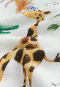 Bomuldsstof med giraffemotiv i gule og brune pletter. Baggrunden indeholder grønne blade og andre abstrakte elementer i bløde farver.