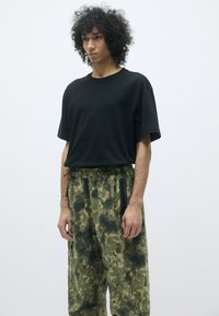 Zwarte katoenen t-shirt met een relaxed fit, gecombineerd met groene broek met camouflagedessin, voorzien van een elastische tailleband en zijzakken met rits.