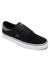 Crne suknje skate tenisice s bijelim gumenim potplatom, s niskim dizajnom i crnim vezicama. Uključuje logo oznaku na jeziku.