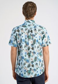 Korte mouw shirt van lichtblauwe stof met een bloemen- en bladerenpatroon in groen, blauw en beige, met een achterste schouderpas en een gebogen zoom.