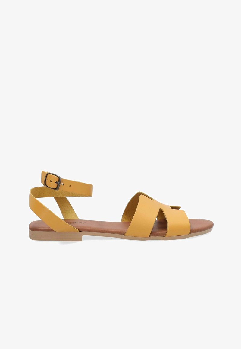Žluté kožené sandály s otevřenou špičkou a vyřezávaným designem, s nastavitelným páskem kolem kotníku a nízkým hnědým podpatkem. Hladká textura.