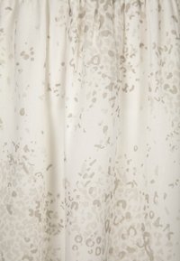 Lehká, krémová látka s jemným abstraktním béžovým vzorem. Textura se zdá hladká a volně splývá, má elastický pas.