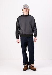 Black sweatshirt with round neck, fitted cuffs, and loose fit. Navy blue straight-leg pants. Gray cap with assorted embroidery. Brown boots.