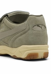 Sneaker en daim vert avec une semelle en caoutchouc beige, présentant une bande accent gris et un petit logo près du talon. Tige texturée et col rembourré.
