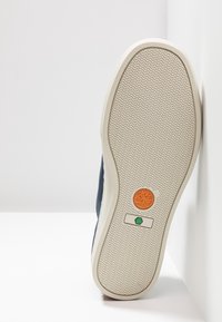 Marinblå sko med en texturerad beige gummisula, prydd med en orange träd-logotyp och en grön indikator. Slät sidodesign och rundad form.