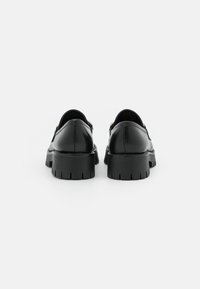 Black leather shoes featuring a chunky sole with deep notches, smooth finish, and rounded back design. No visible hardware accents.