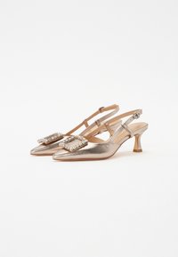 Fémes arany slingback sarkú cipő, hegyes orral, díszes, drágakövekkel ékesített csattal a felsőrészen és közepes magasságú tömbsarkal.